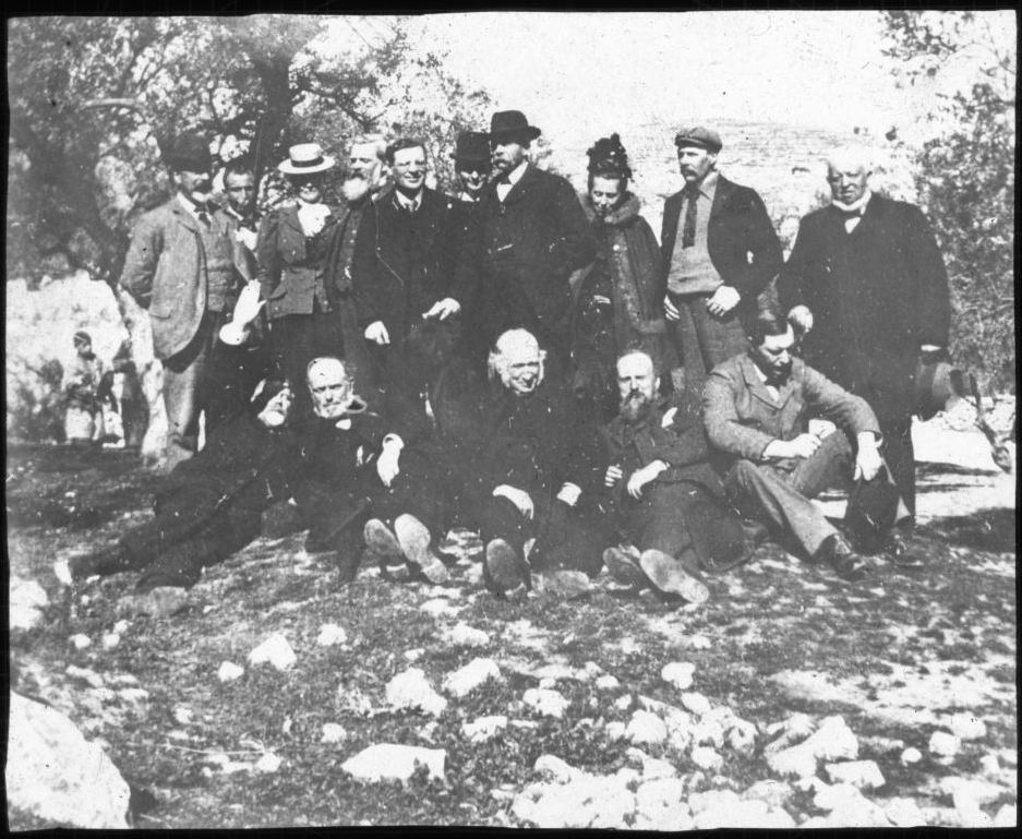 Unlabelled slide showing a group – presumably the travel party – of 15 (13 men and two women) in an olive grove with locals looking on in the background. One of the men has his hand up either to shield from the sun, or make some astrological point, RCB Library Stillorgan Lantern Slides, Europe–Holy Land travel