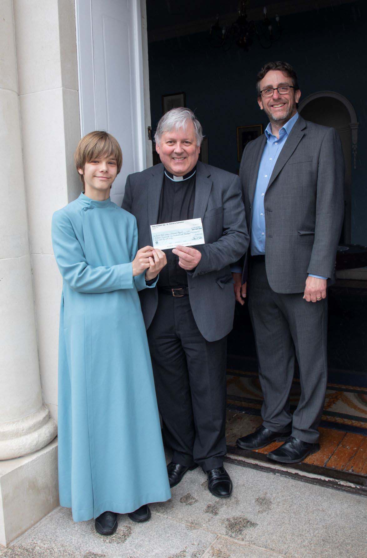 A chorister, Dean of Saint Patrick's Cathedral, the Very Revd Dr William Morton, and Master of Music Stuart Nicholson holding the cheque for Irish Red Cross.